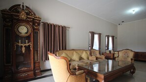 A living room with a large wooden clock, a sofa, and a glass coffee table. - Hotel O Wisma Ray Syariah (Bandar Lampung)