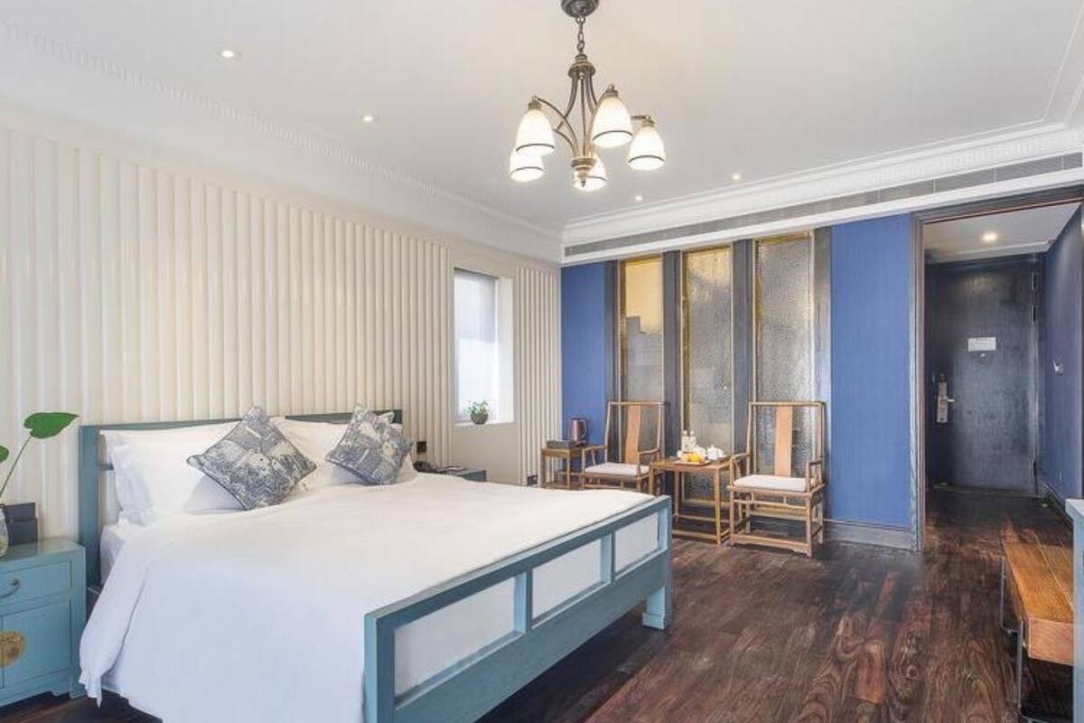 A bedroom with a bed, bedside tables, a chandelier, and a view of a hallway.
