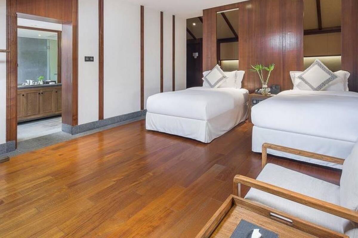 A modern hotel room with two beds, wooden flooring, and a view of the kitchen.