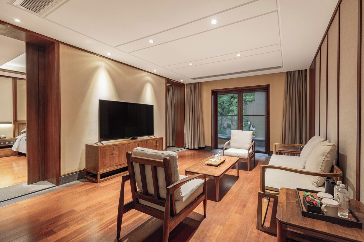 A hotel room with a flat-screen TV, wooden furniture, a sofa, a coffee table, and a sliding glass door to the outside.