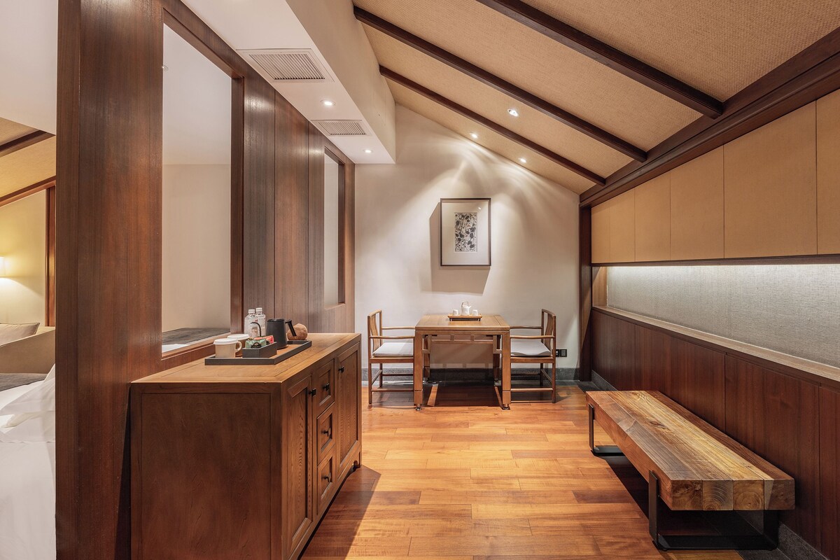 A room with a wooden bench, a table with chairs, and a framed picture on the wall.