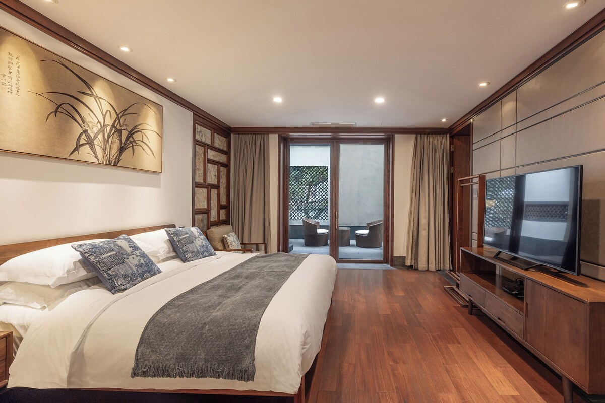 A modern bedroom with a large bed, a television, and a sliding glass door leading to an outdoor area.
