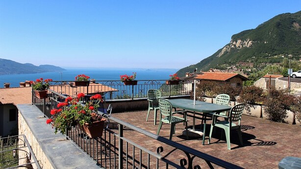 A terrace with a table and chairs, overlooking a coastal landscape with a view of the sea and mountains. - Stella: with huge lake view balcony (Tignale)