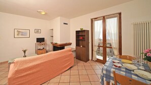 A living room with a sofa, a television, a fireplace, and a dining area with a table set for four. - Stella: with huge lake view balcony (Tignale)