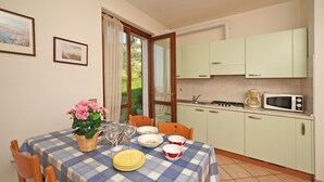 A dining area with a table set for four, a kitchen with light green cabinets, a gas stove, and a microwave. - Stella: with huge lake view balcony (Tignale)
