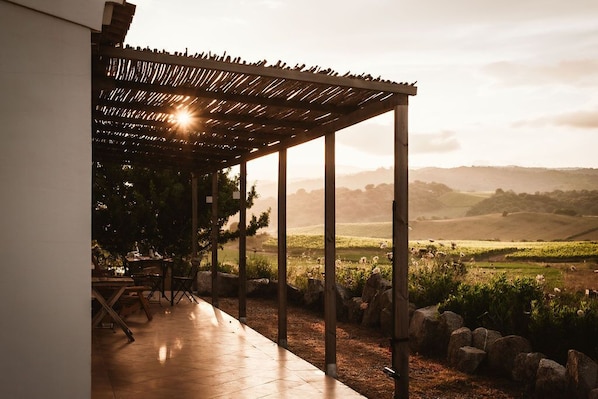 An outdoor patio area with a pergola, stone seating, and a view of rolling hills in the distance.