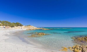 Une plage aux eaux turquoise et limpides, bordée de rochers et d’une étendue de sable.