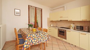 Un comedor con una mesa cubierta con mantel estampado de frutas, sillas de madera y un florero con flores.