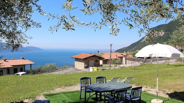 Una terraza con mesa y sillas, con vistas a la costa, casas y una estructura abovedada blanca.