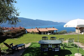 A terrace with a table and chairs, overlooking a lake and mountains. - Luna: lake view apartment with two bedrooms (Tignale)