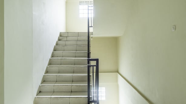 Un escalier avec une rampe en métal, menant à un palier doté d’une fenêtre.