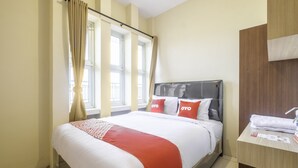 Une chambre d’hôtel avec un lit, une tête de lit en bois, une fenêtre avec des rideaux et une petite table sur laquelle est posée une serviette.