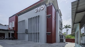Un bâtiment arborant une enseigne « OYO » bien visible, une entrée sécurisée par un portail et un espace de stationnement où sont garées des motos.