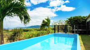 Una piscina con superficie de agua azul cristalina, rodeada de vegetación exuberante y una terraza de madera.