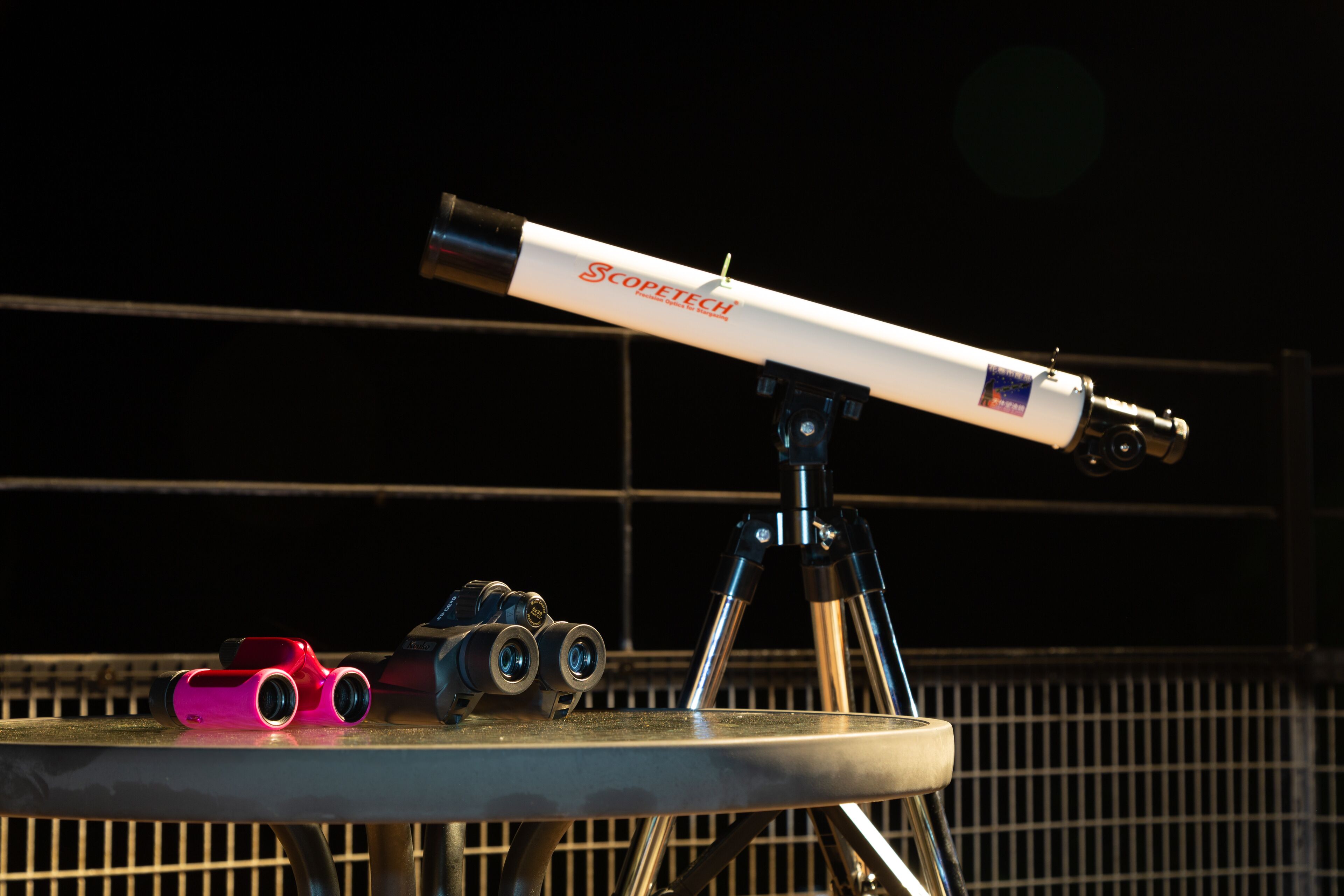 A telescope on a tripod with a metal table in the foreground.