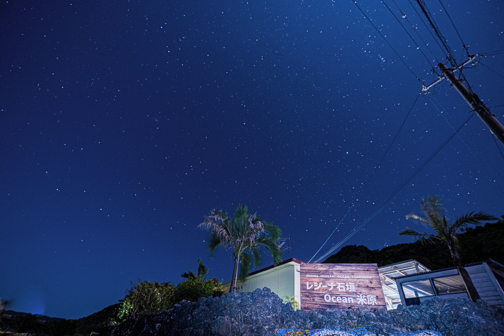 A starry night sky over a building with a sign in Japanese.