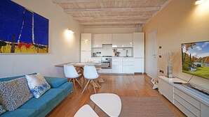 Een moderne woonkamer met een blauwe bank, witte stoelen en een tv op een dressoir.