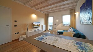Een moderne woonkamer met een houten plafond, een aan de muur bevestigde televisie, een bank, een eettafel met een placemat en een schilderij.