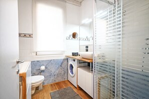 A modern bathroom with a toilet, washing machine, and a glass shower enclosure. - L'Orologio with lakeview balcony in centre of Salò (Salò)