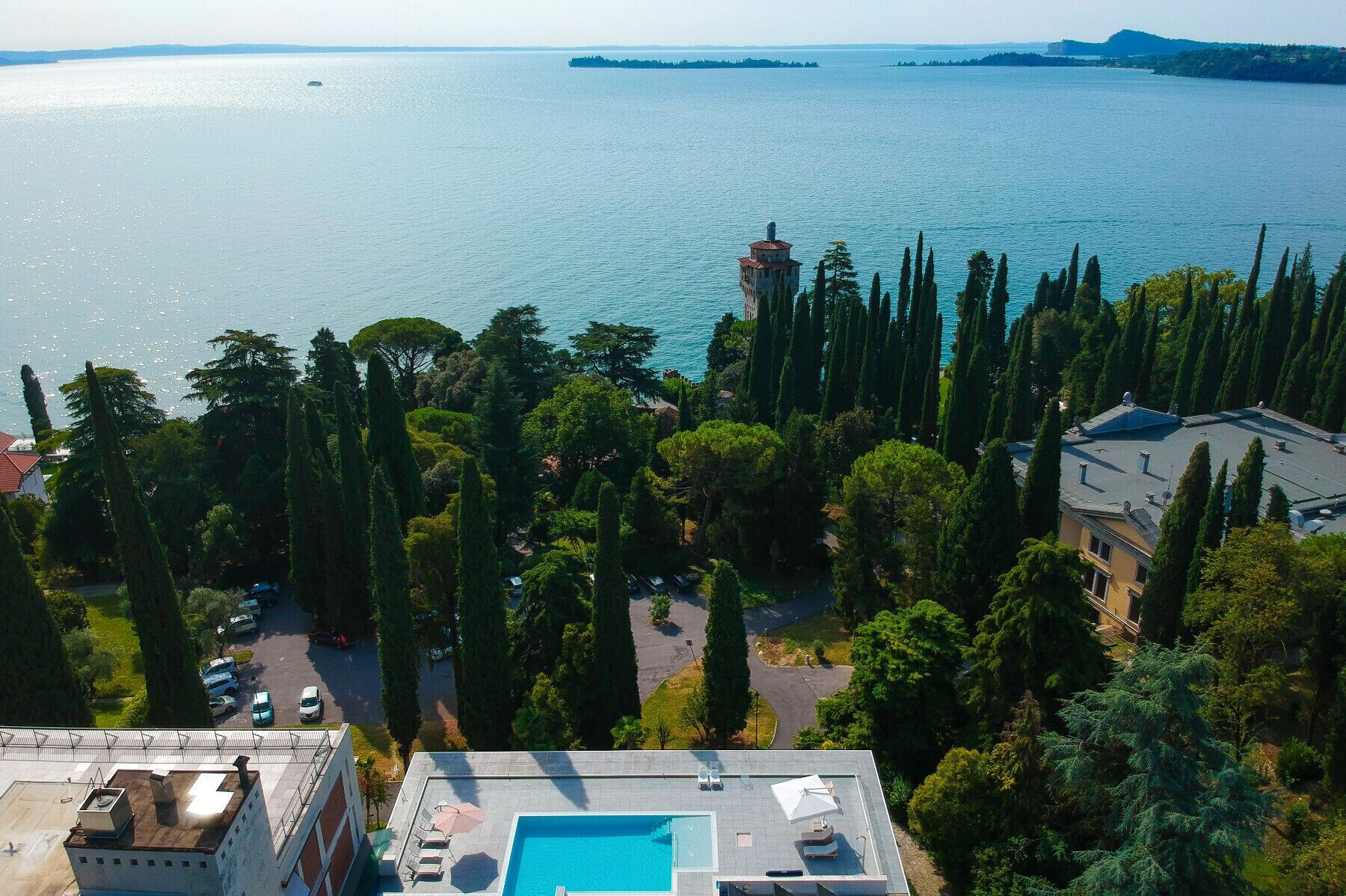 Una piscina en la azotea con vista al mar, rodeada de árboles altos y edificios.