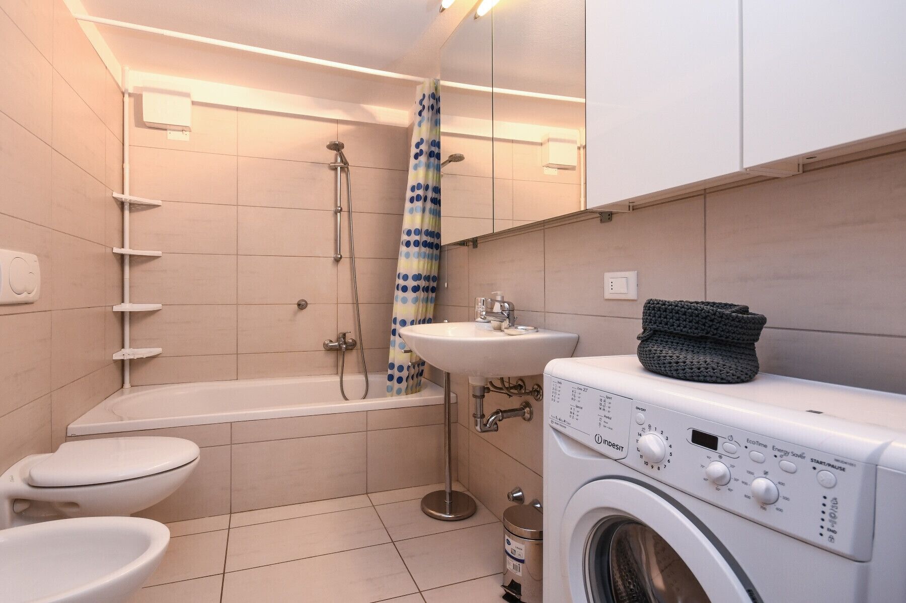 Een kleine badkamer met toilet, wastafel, douche en wasmachine.