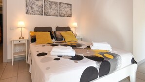 Een netjes opgemaakt bed met een beddekleed met patroon, twee bedlampjes en een klein nachtkastje met een lamp.