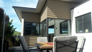 A modern outdoor seating area with a table and chairs, large windows, and a view of the landscape.