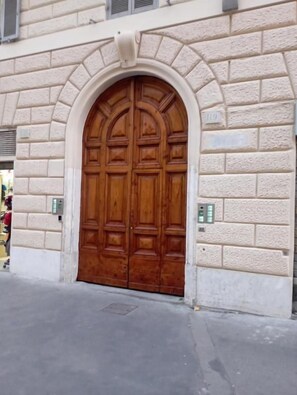 Une grande porte en bois à arc, avec une façade en briques, une petite fenêtre au-dessus et une entrée au niveau du sol.