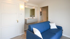 A modern living room with a blue sofa, white pillows, a white door, and a bathroom with a mirror and sink. - Cupido: with big lake view balcony in Gardone Riviera (Gardone Riviera)