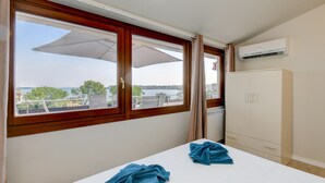 A room with a bed, a wardrobe, and a window with a view of a body of water and trees. - Cupido: with big lake view balcony in Gardone Riviera (Gardone Riviera)