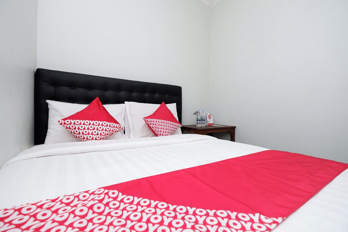 A neatly made bed with a white and red bedspread, two white pillows, and two red pillows with a repeated pattern.