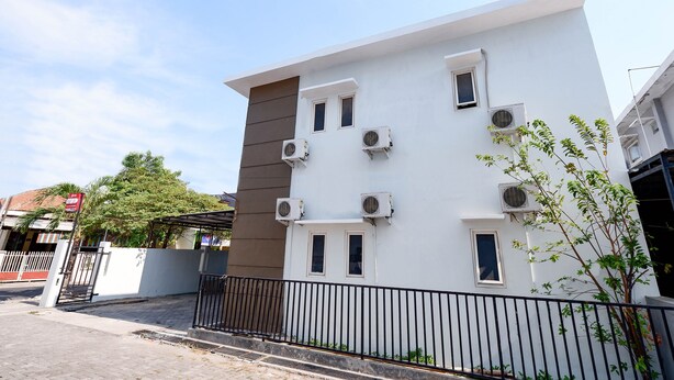 A modern building with multiple air conditioning units, a gated entrance, and a small tree in front. - Hotel O Palebon Residence (Semarang)