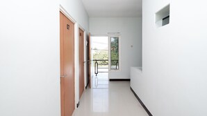 A hallway with wooden doors, a window, and a white wall. - Hotel O Palebon Residence (Semarang)