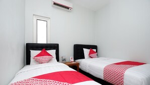 A hotel room with two beds, each with a black headboard and red and white bedding. There is a small wooden nightstand between the beds with a water bottle and a tissue box. - Hotel O Palebon Residence (Semarang)