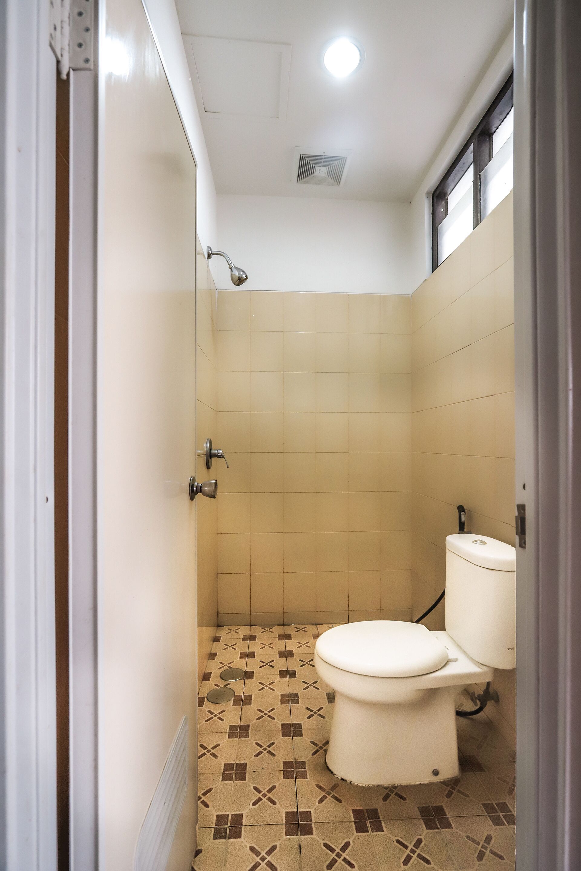 Een compacte badkamer met toilet, douche en betegelde vloer.