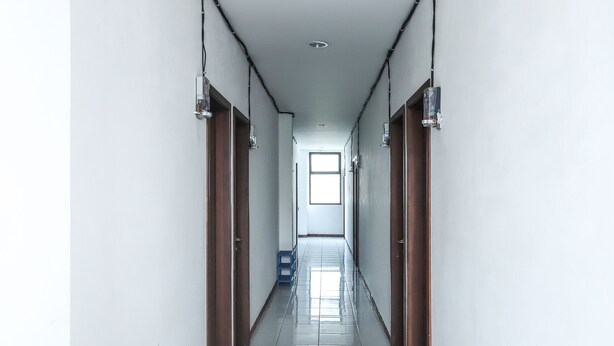 Un pasillo largo y estrecho con puertas a ambos lados, que conduce a una habitación luminosa con un ventanal grande.