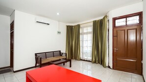 Una habitación con una mesa roja, un banco de madera, una puerta marrón y cortinas verdes.