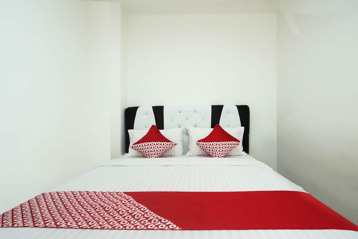 A bed with a white headboard, two red pillows, and a red and white patterned bedspread.