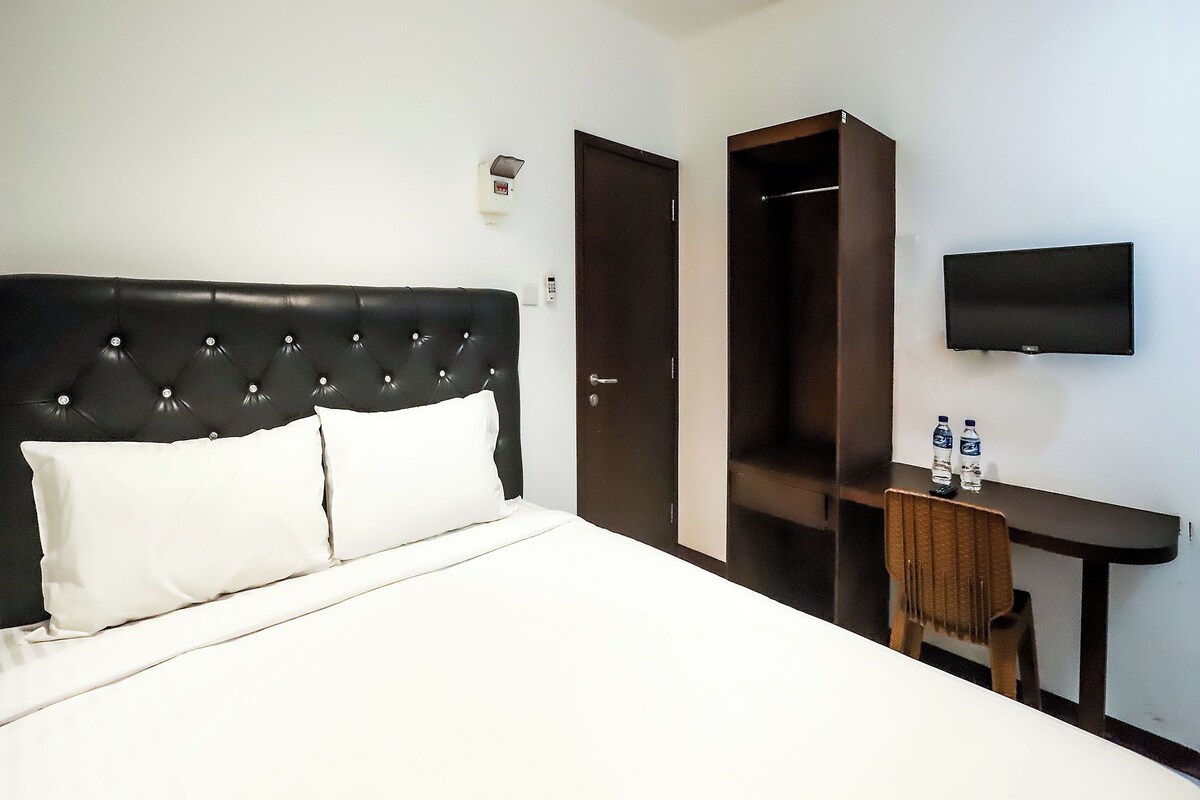 Habitació d'hotel amb un llit gran, un escriptori, una cadira, un armari i un televisor penjat a la paret.