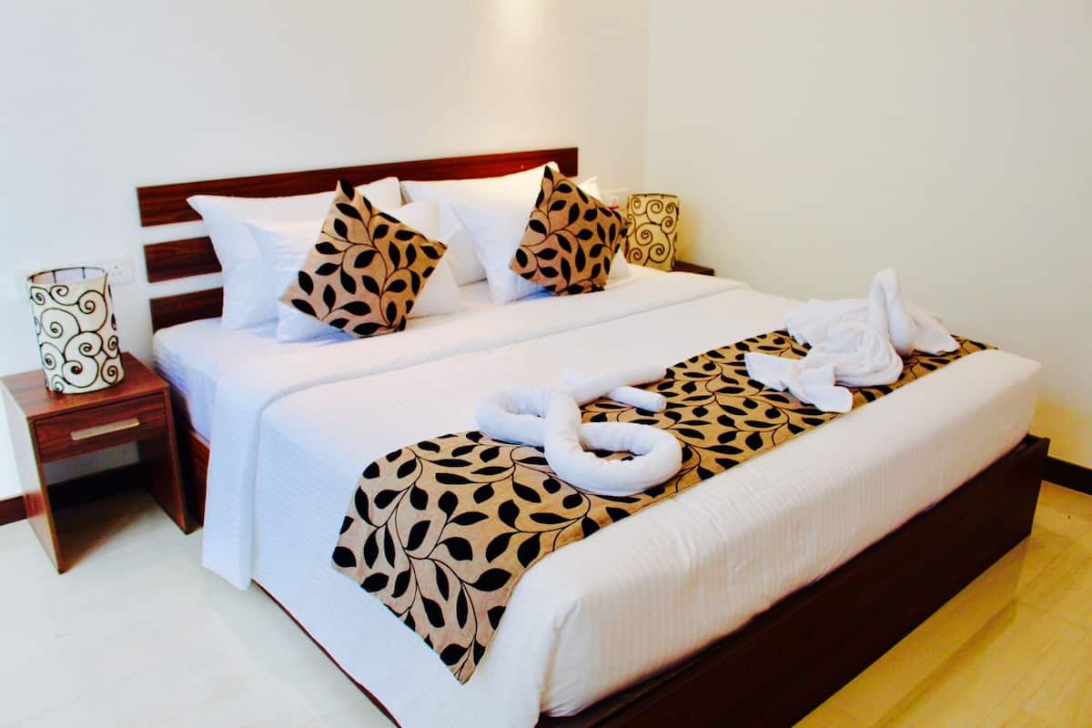 A double bed with a leaf-patterned bedspread, white pillows, and a wooden headboard. There are two bedside tables with lamps and a decorative pillow.