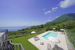 A pool area with lounge chairs and umbrellas, surrounded by greenery and a view of the sea. - Cà Bianca sopra: in the middle of the nature with stunning lake view (Toscolano-Maderno)