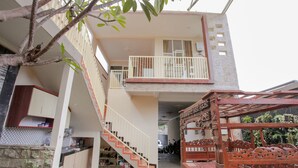 A two-story building with a balcony on the upper floor, a staircase leading to the upper level, and a wooden bed frame visible on the ground floor. - OYO 1692 Villa Akbar 3 (Batu)