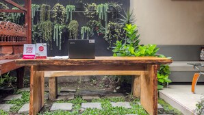 A wooden table with a laptop, surrounded by potted plants and a QR code sign. - OYO 1692 Villa Akbar 3 (Batu)