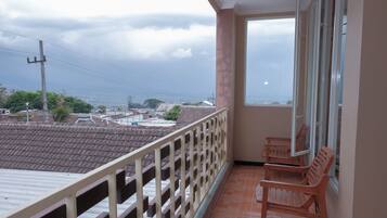 A balcony with a view of a cityscape, a wooden bench, and a tiled floor.