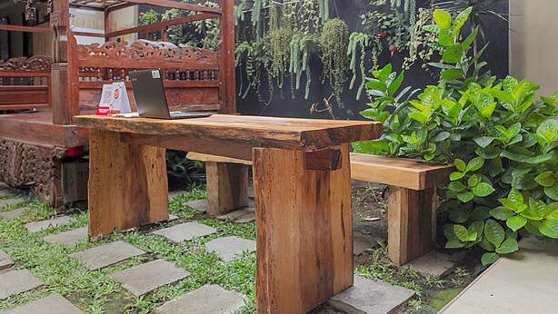 A wooden outdoor seating area with a laptop on a table, surrounded by lush greenery and a hanging plant display. - OYO 1692 Villa Akbar 3 (Batu)