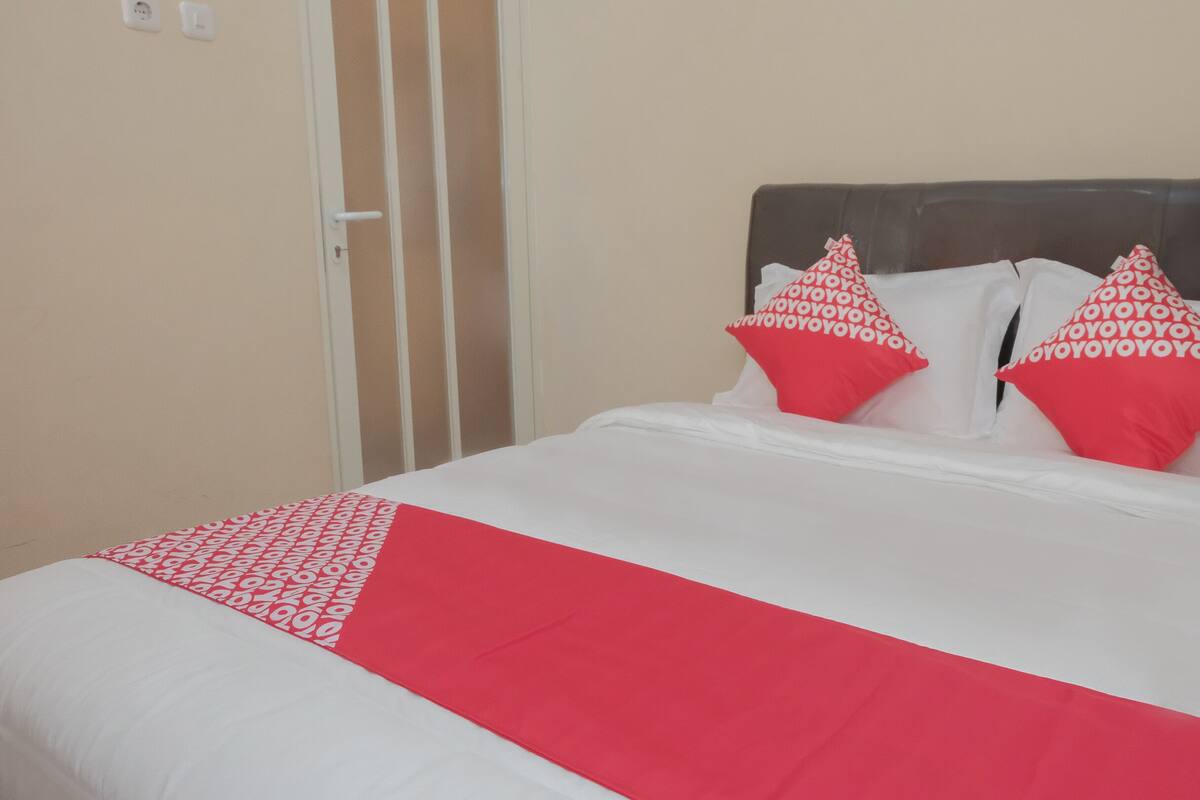 Una cama con ropa de cama blanca y roja, dos almohadas rojas con letras blancas, y un cabecero blanco.
