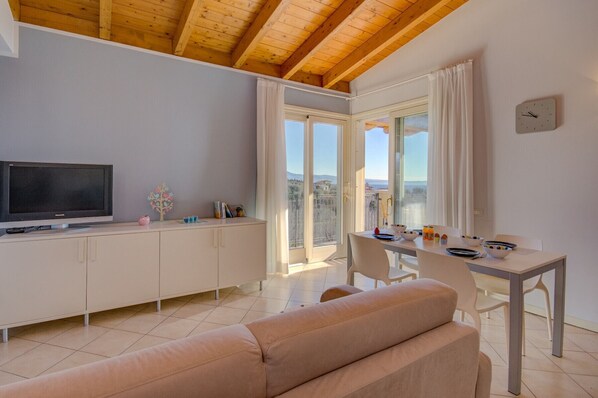 Una sala de estar moderna con un sofá, un televisor, una mesa de comedor con sillas y un balcón con vistas.