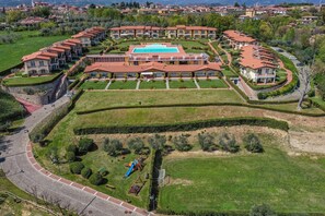 An aerial view of a resort with multiple buildings, a central swimming pool, and well-maintained gardens.