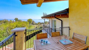 A balcony with wooden furniture, a table, and chairs, overlooking a scenic landscape with trees and a body of water. - Fedra: with lake view balcony naer to the lake (Manerba del Garda)