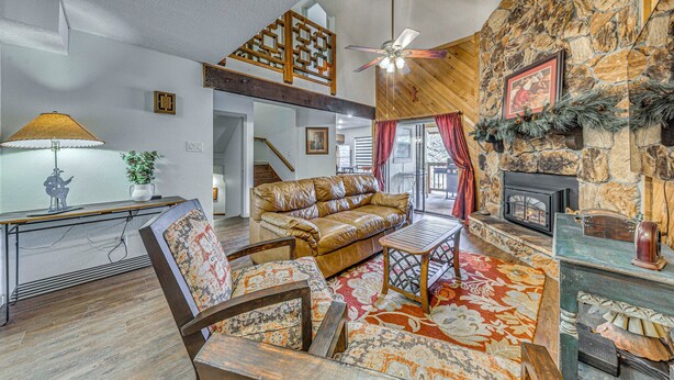 A cozy living room with a stone fireplace, a wooden ceiling fan, and a leather sofa. - Spacious Ruidoso Retreat w/ Hot Tub & 2 Kitchens! (Ruidoso)
